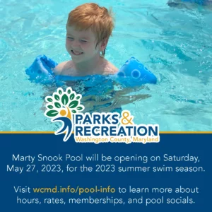 A happy child with red hair smiling and wearing floaties while swimming at marty snook park. visit wcmd.info/pool-info to learn about pool hours, rates, memberships, and socials.