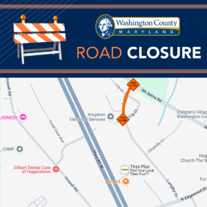 Map and graphic from Washington County, Maryland, showing a road closure on a section of Langley Drive between Lily Court and Mt Aetna Road. The closure is marked with orange "ROAD CLOSED" signs. Nearby landmarks include Denny's, Tires Plus, Gilbart Dental Care of Hagerstown, and Kingdom Electrical Services. The map also shows Hwy 40 W, Crest View Ave, Howell Rd, and Chantilly Ct. The top of the image features a blue banner with the Washington County seal and the text "ROAD CLOSURE" alongside an illustration of a construction barrier.